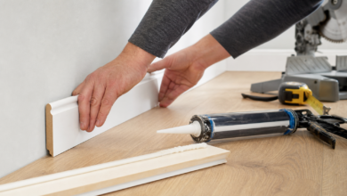 Weiße Fußleiste wird mit Montagekleber an Wand und Holzboden angebracht