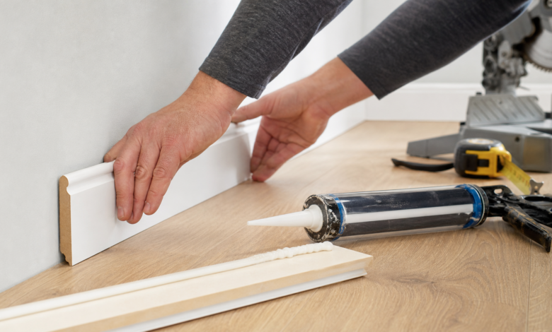Weiße Fußleiste wird mit Montagekleber an Wand und Holzboden angebracht